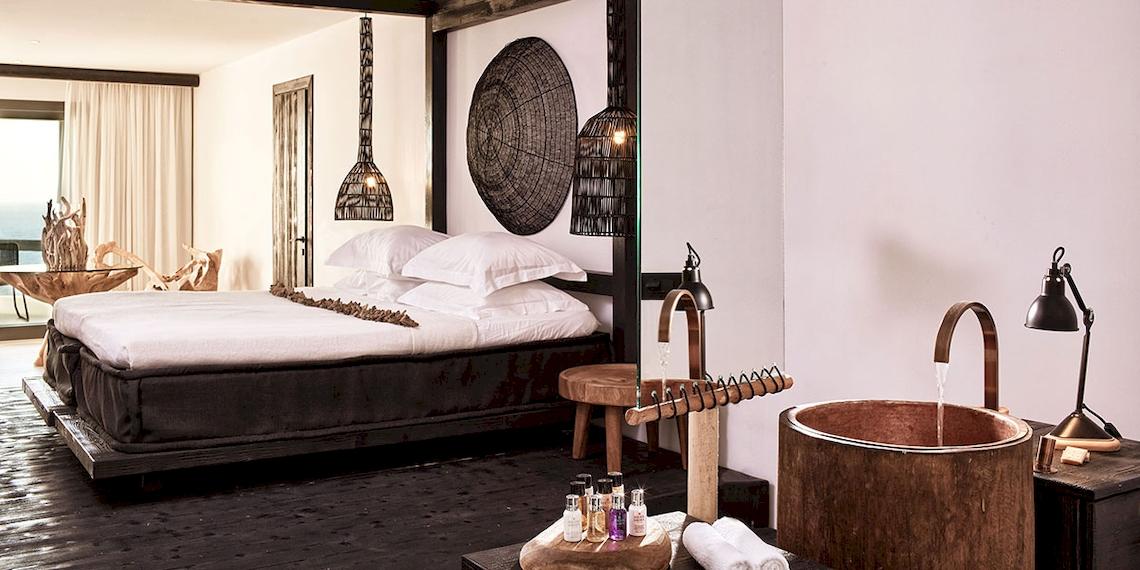 Schlafzimmer im Myconian Utopia Resort mit Bett, Lampen, Badewanne und Aussicht auf das Meer.