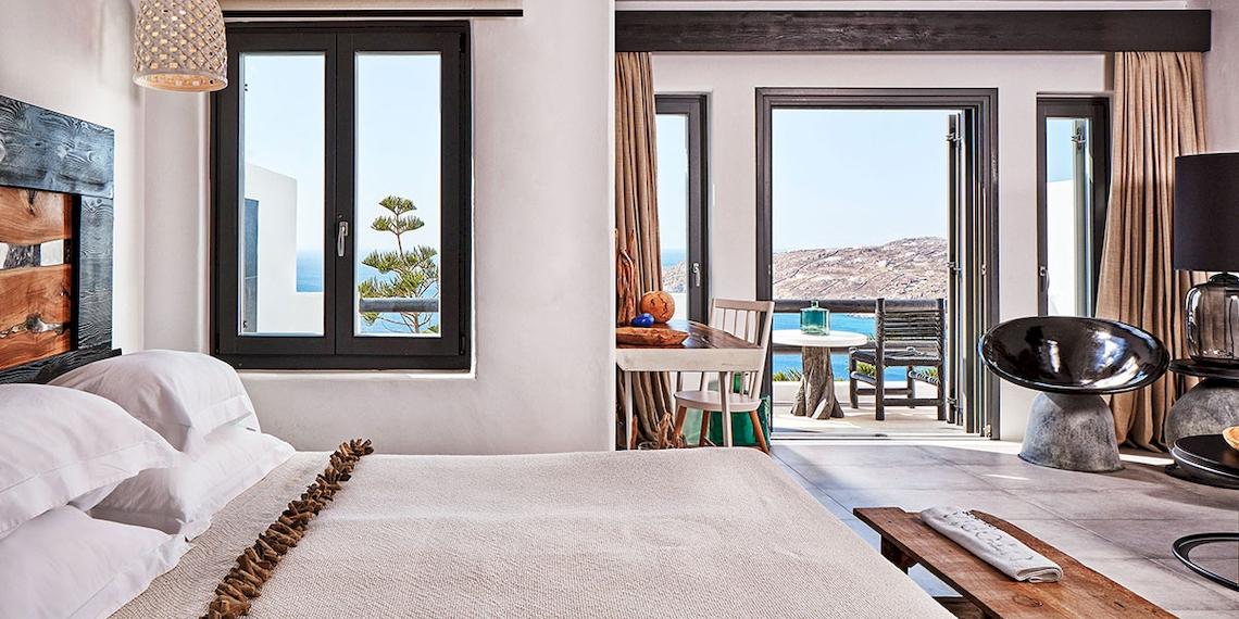 Schlafzimmer im Myconian Utopia Resort mit Meerblick, Fenster, Balkon, Tisch, Stühle und Lampen.