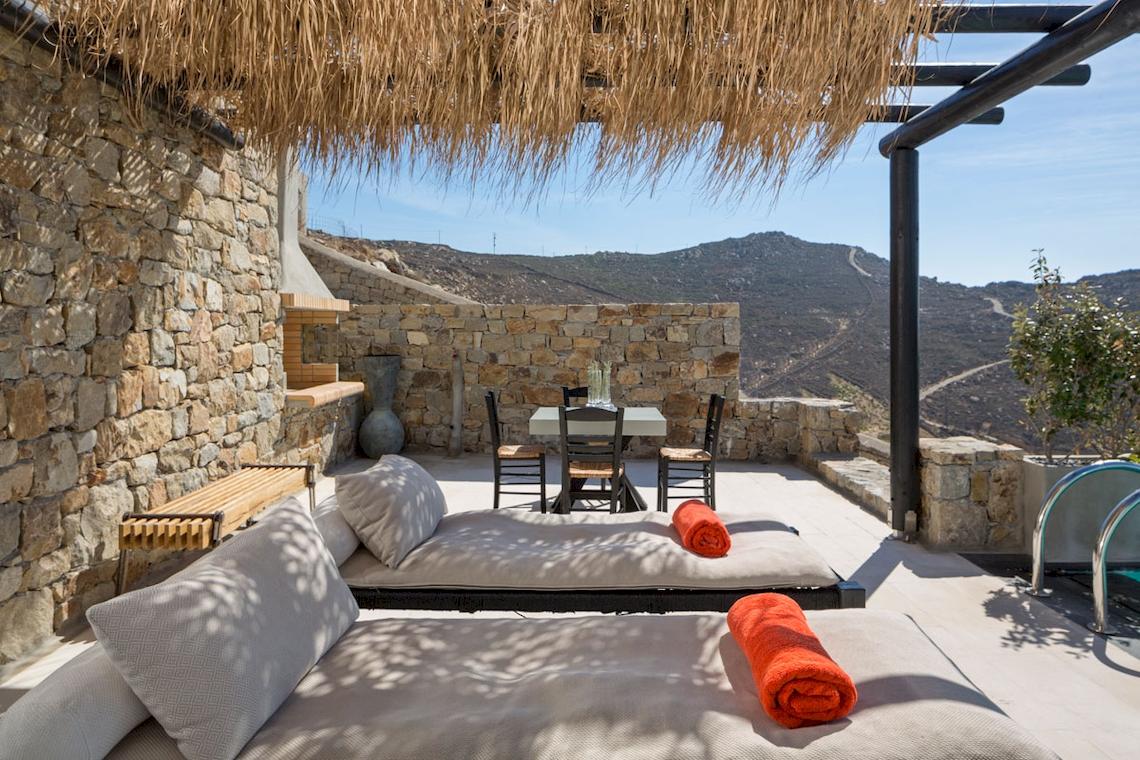 Terrasse des Myconian Utopia Resorts mit Loungebetten, Tisch und Blick auf Berge