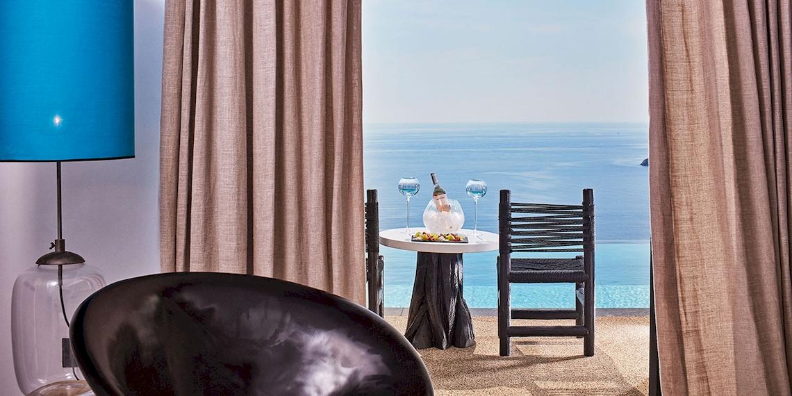 Blick aus dem Hotelzimmer auf den Ozean mit einem Tisch und zwei Stühlen.