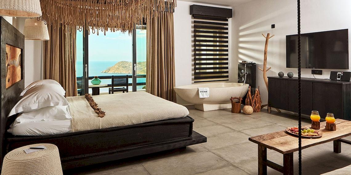 Myconian Utopia Resort Zimmer mit Meerblick, Bett, Badewanne, Fernseher, Tisch mit Getränken, Aussicht auf das Meer und Inseln.