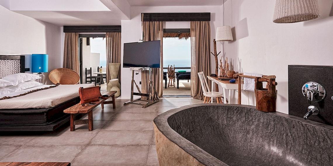 Ein modernes Hotelzimmer mit einem großen Bett, Fernseher, Schreibtisch und Badewanne mit Meerblick.