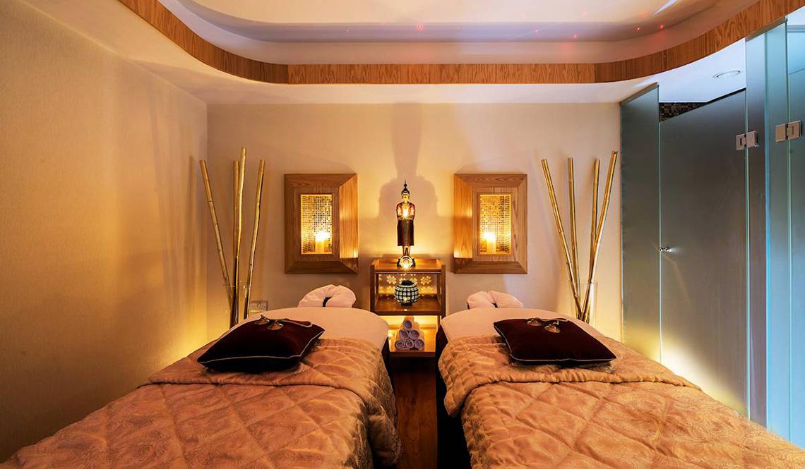 Massage-Behandlungsraum im Athena Royal Beach Hotel mit zwei Betten und Buddha-Statue.