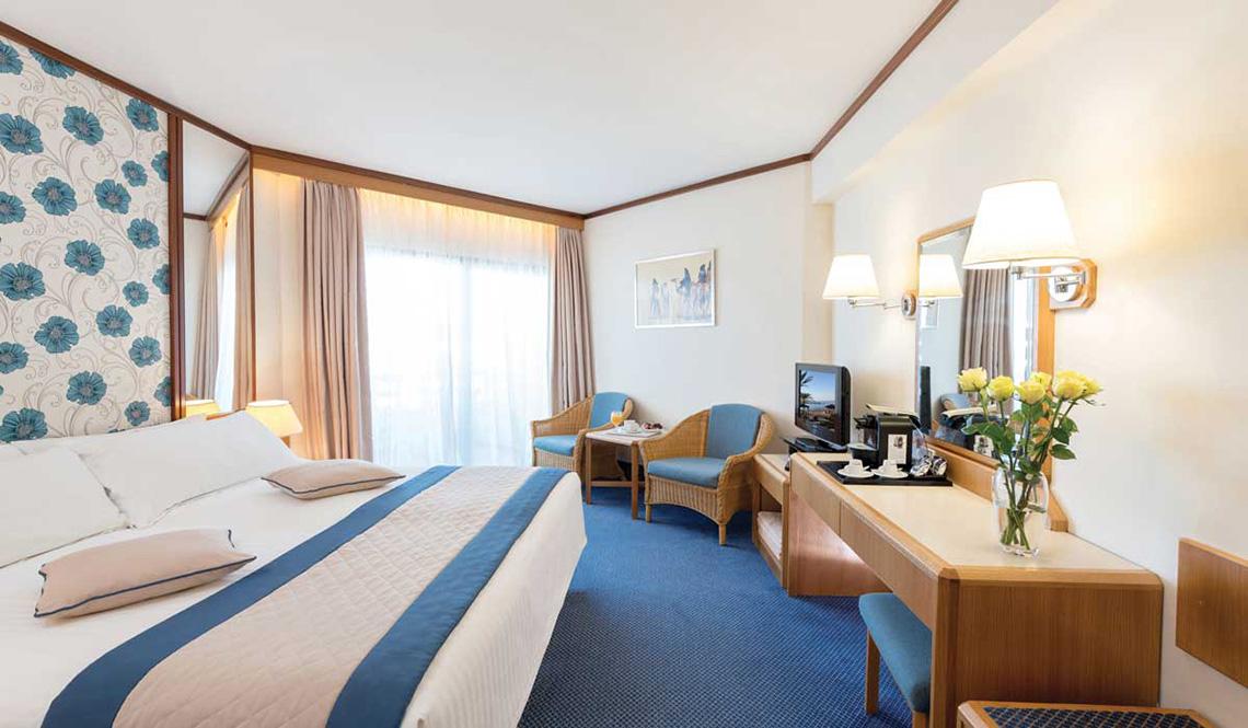 Zimmer im Athena Royal Beach Hotel mit Bett, Fernseher und Schreibtisch