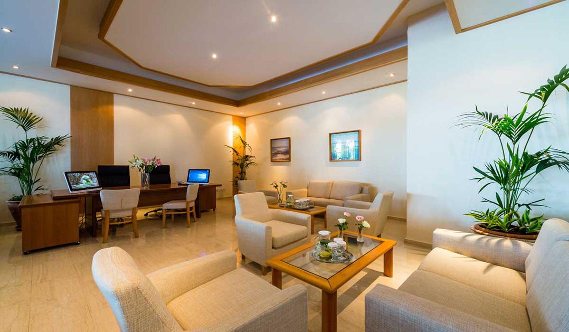 Lobby-Bereich im Athena Royal Beach Hotel mit Möbeln, Pflanzen und Monitoren.