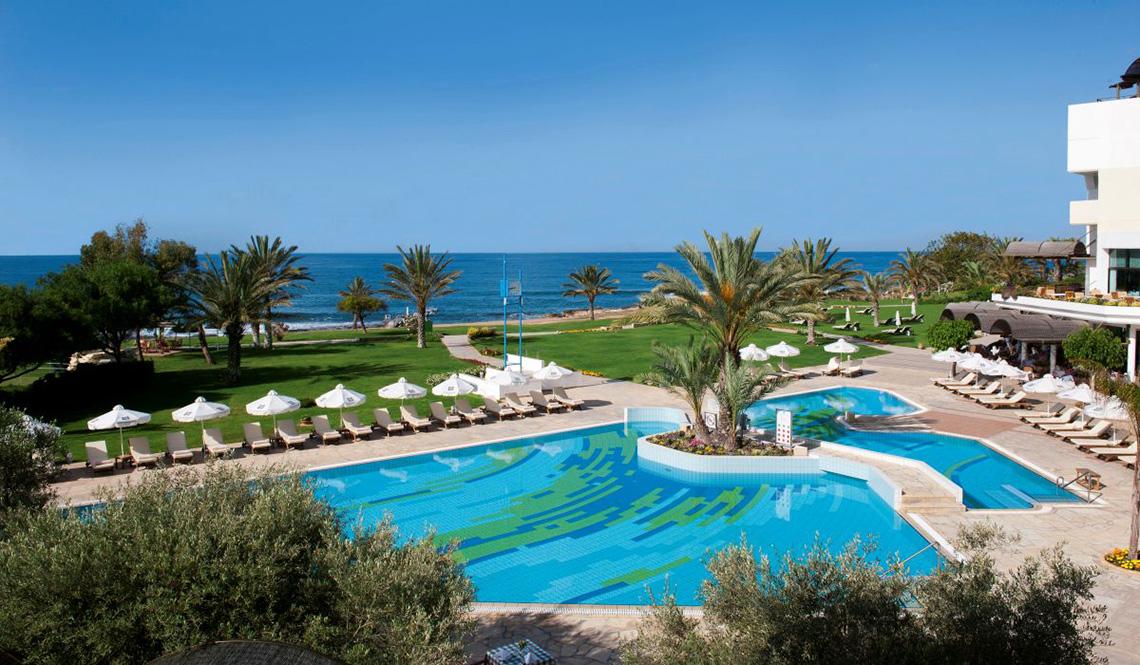 Oberirdischer Pool des Athena Royal Beach Hotels mit Sonnenliegen und Palmen