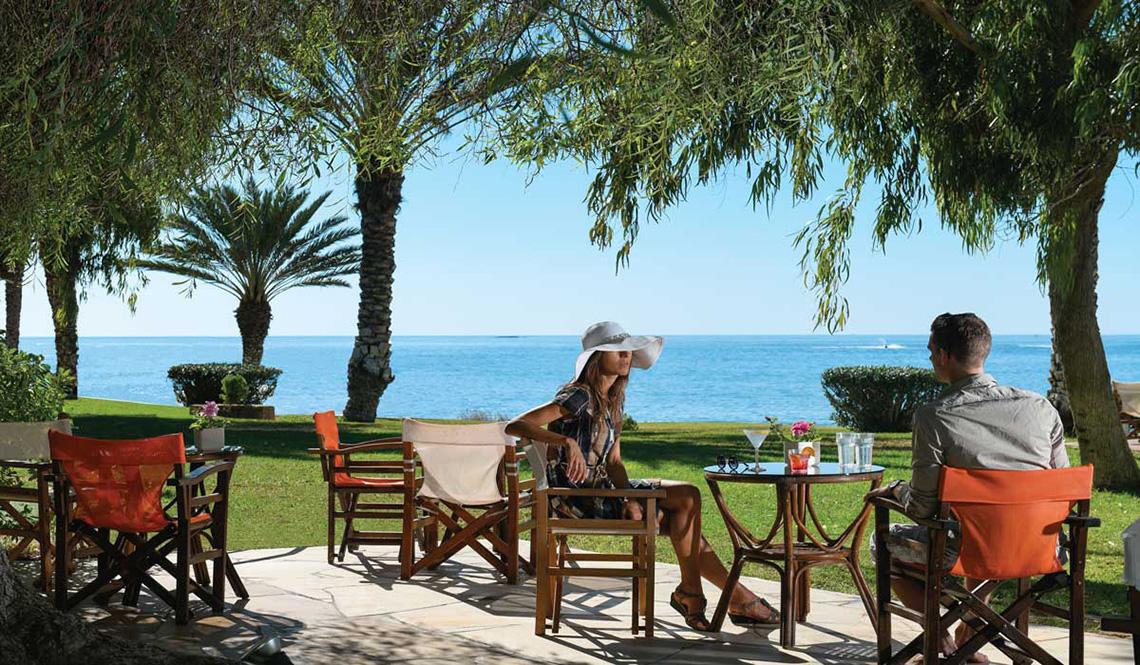 Zwei Personen sitzen auf Stühlen mit Blick auf das Meer im Athena Royal Beach Hotel.