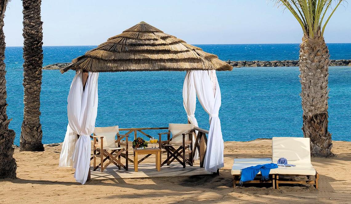 Sitzplatz im Athena Royal Beach Hotel mit Blick auf das Meer und weißen Vorhängen.