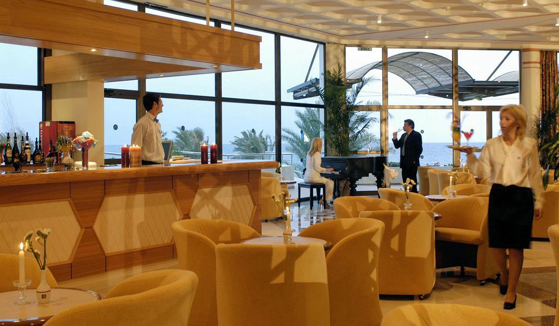 Bar im Athena Royal Beach Hotel mit Panoramafenstern und Blick auf das Meer.