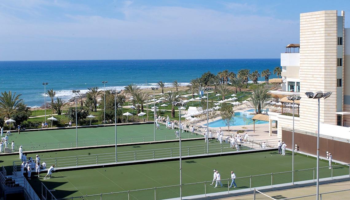Aerial view of the Athena Royal Beach Hotel with outdoor tennis courts and a swimming pool by the ocean.