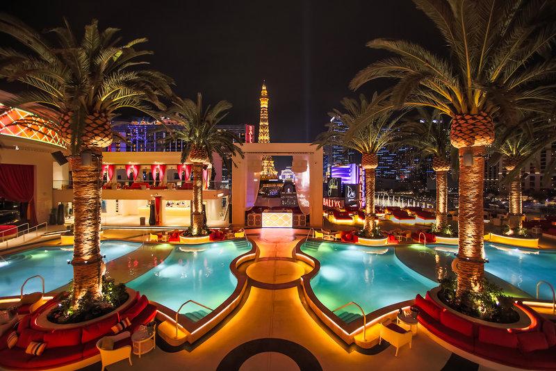 Nachtaufnahme des Poolbereichs des Cromwell Las Vegas Hotel & Casino mit Palmen und beleuchteten Gebäuden im Hintergrund.