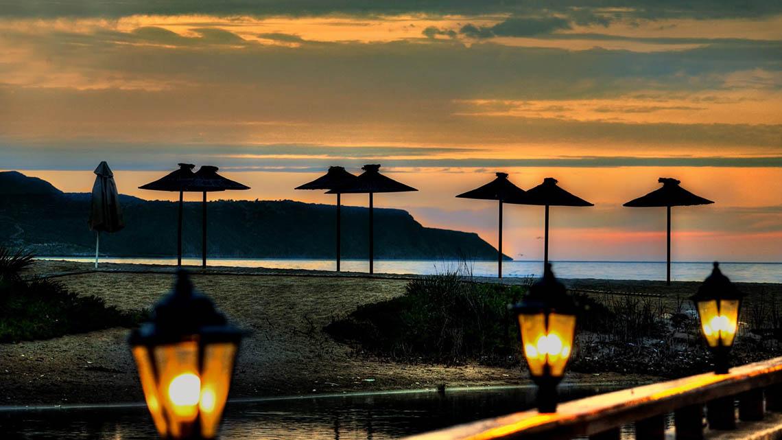 Sonnenuntergang am Kalyves Strand mit Sonnenschirmen auf der Wiese