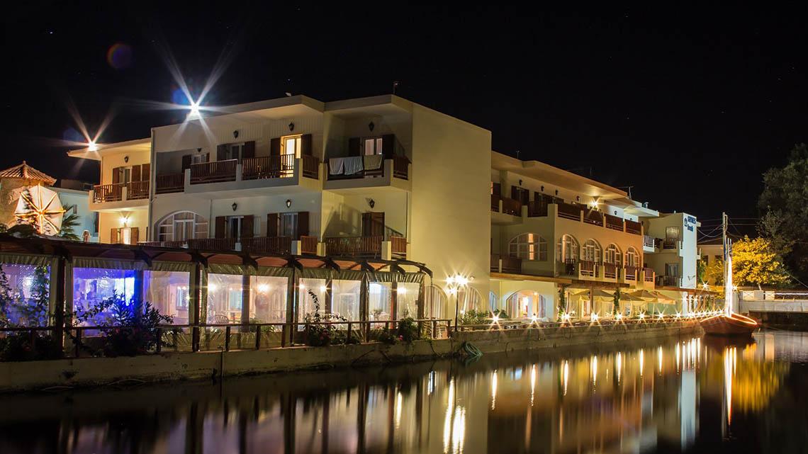 Nachtansicht des Kalyves Beach Hotels mit Beleuchtung und Wasserreflexion.