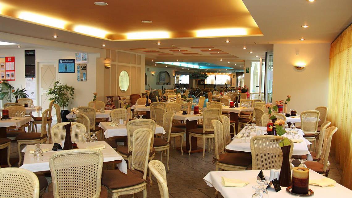 Innenansicht des Restaurants im Kalyves Beach Hotel mit vielen gedeckten Tischen und Stühlen.