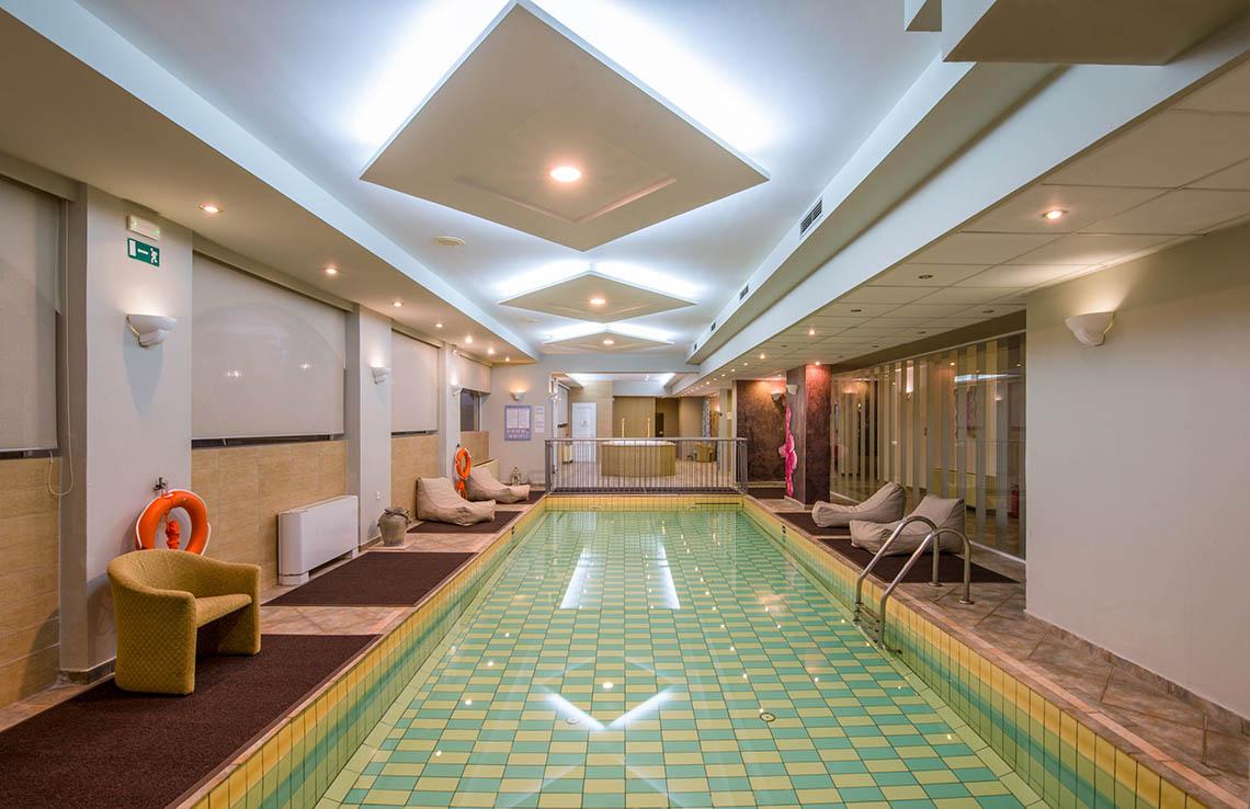 Innenpool des Kalyves Beach Hotels mit gefliesten Wänden und Sonnenliegen.