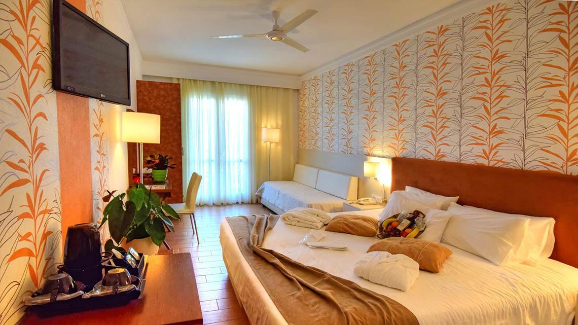 Hotelzimmer im Kalyves Beach Hotel mit Fernseher, Deckenventilator, Bett und Sofa.