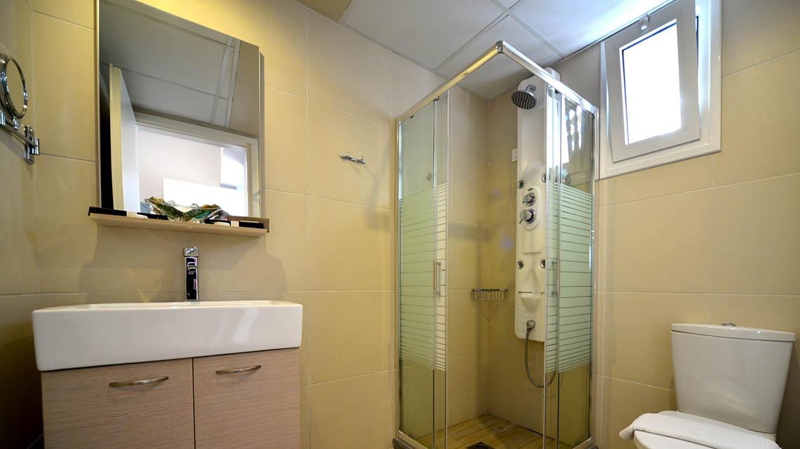 Badezimmer im Kalyves Beach Hotel mit Glasdusche, Waschbecken und Toilette.