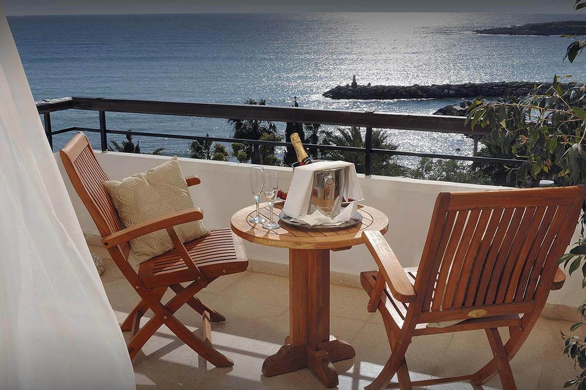 Balkon des Coral Beach Hotel mit Blick auf das Meer und einem Tisch mit Champagner und Gläsern.