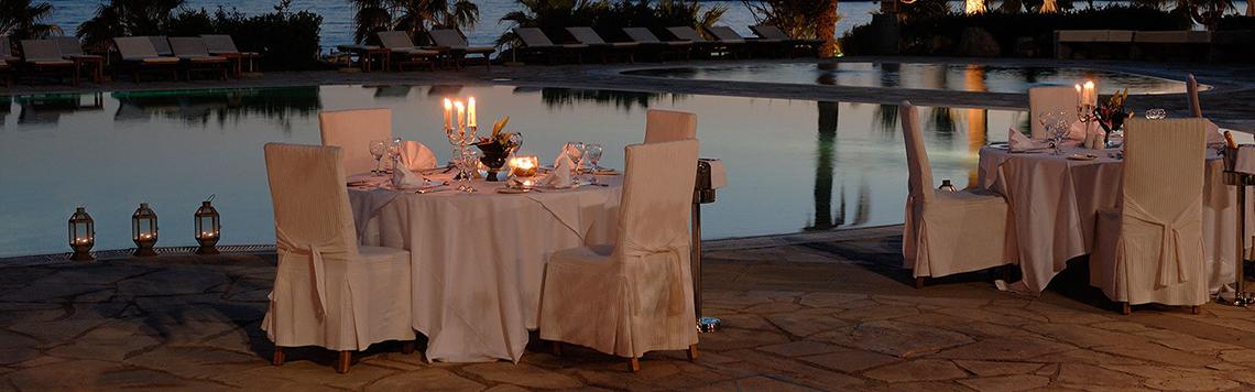 Dinnertische am Pool des Coral Beach Hotel & Resorts mit Kerzen und weißen Tischdecken.