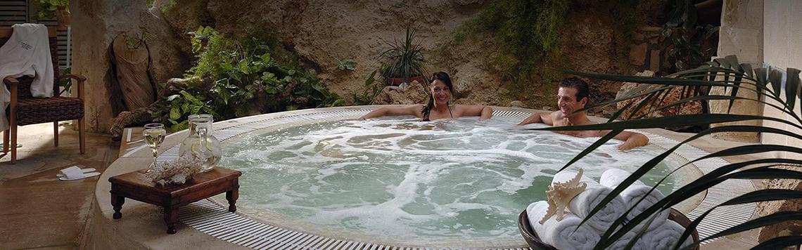 Ein Whirlpool im Freien mit zwei Personen im Coral Beach Hotel & Resorts, umgeben von Pflanzen und einem Tisch.