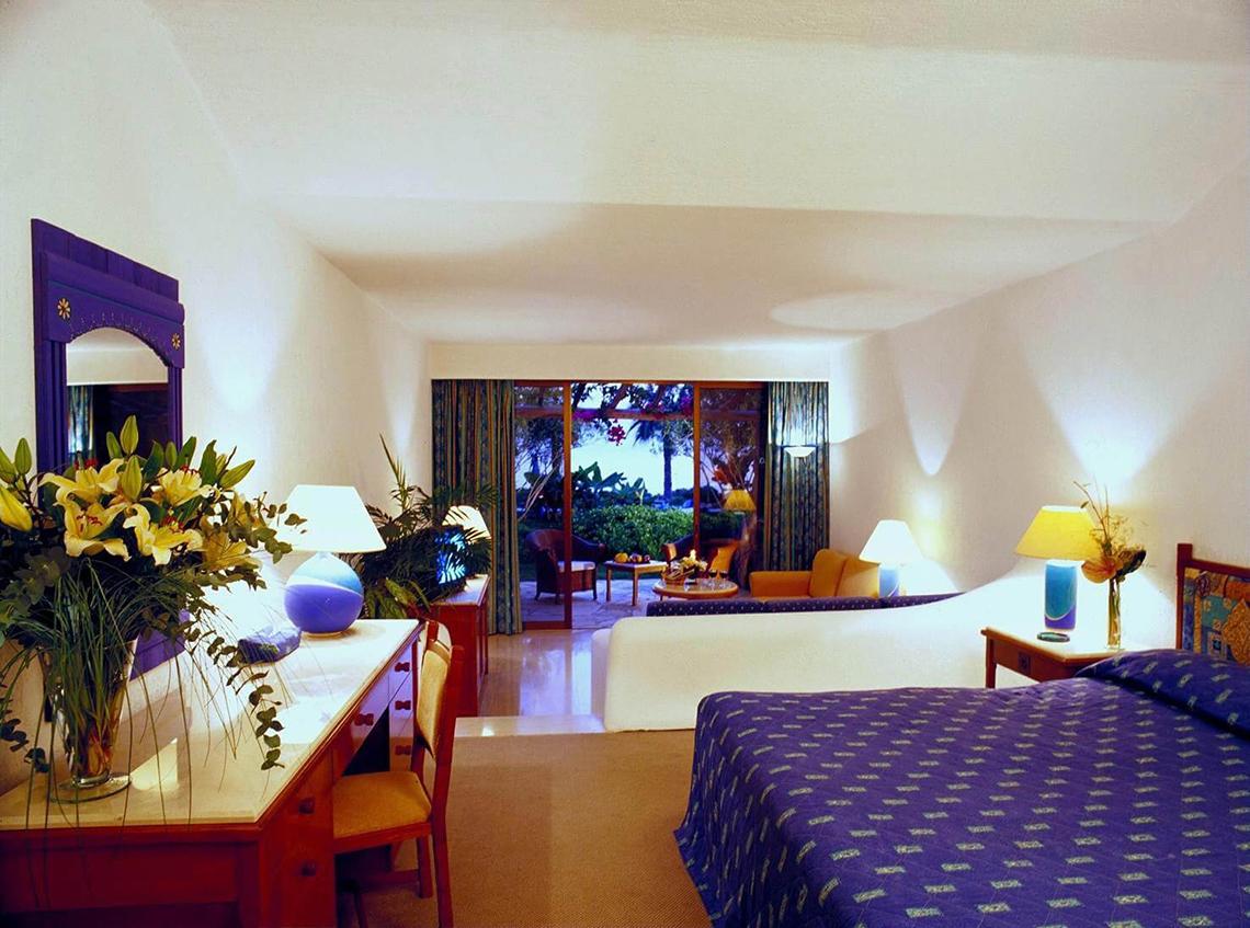 Innenansicht eines eleganten Zimmers im Coral Beach Hotel & Resorts mit Bett, Schreibtisch und Balkon