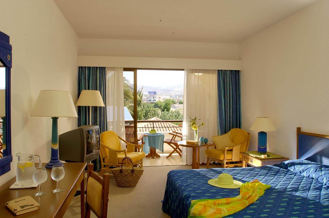 Zimmer im Coral Beach Hotel & Resorts mit Balkon, Fernseher und gemütlichen Möbeln.