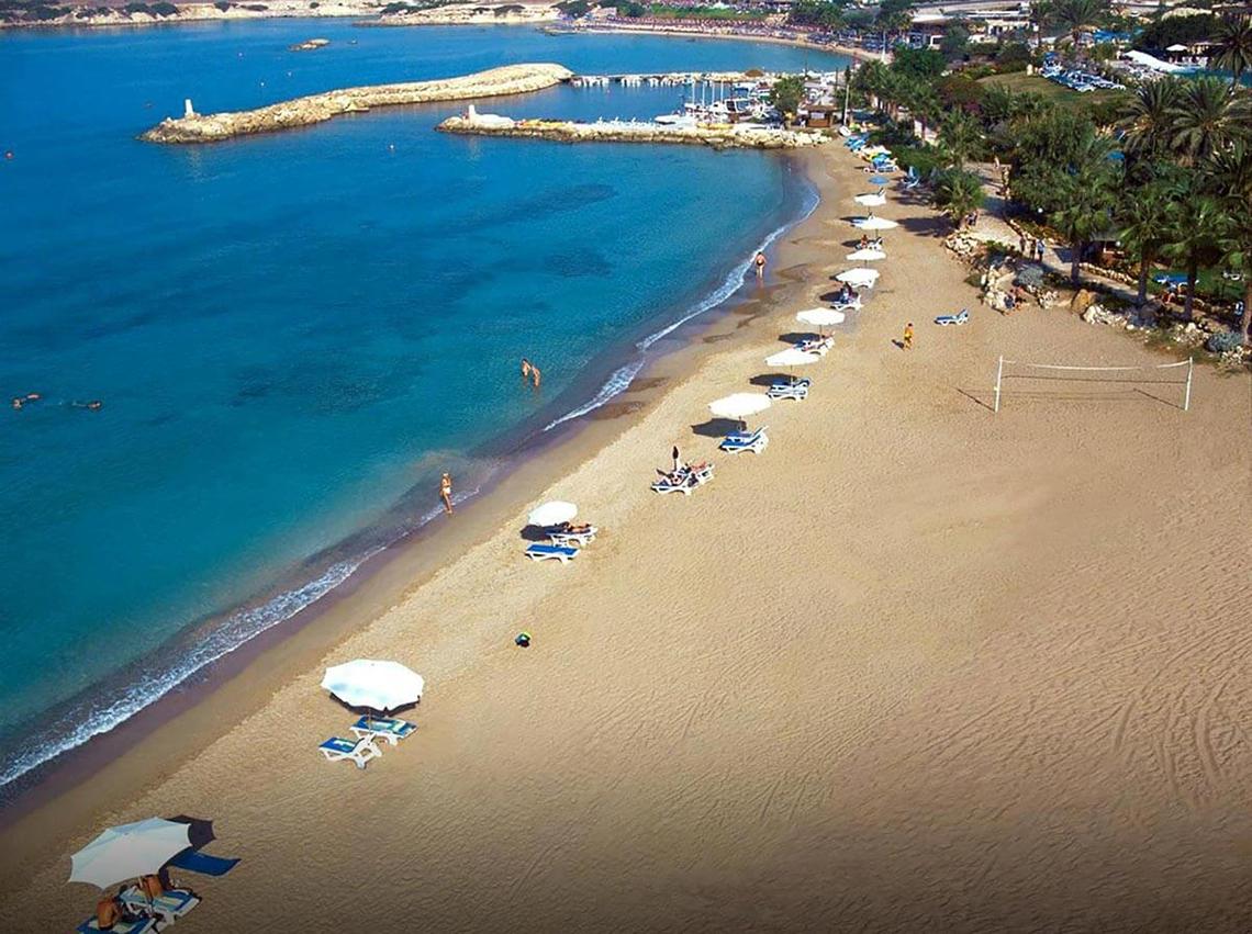 Luftaufnahme des Coral Beach Hotel & Resorts Strands mit blauem Wasser und Sonnenschirmen