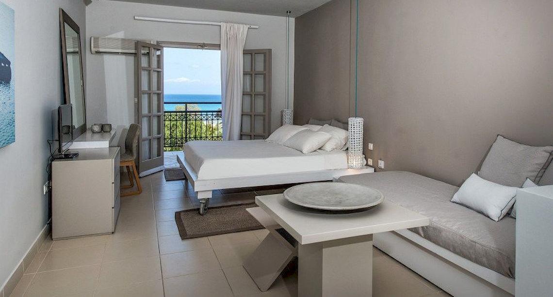 Zimmer im Bay Hotel mit Balkon, zwei Betten, Schreibtisch, Fernseher, und Blick auf das Meer.