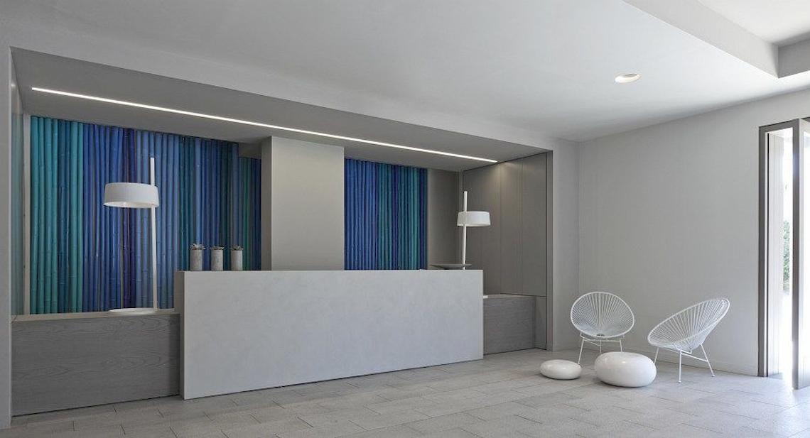 Empfangsbereich des Bay Hotel & Suites mit modernem Design, weißen Möbeln und blauen Vorhängen.