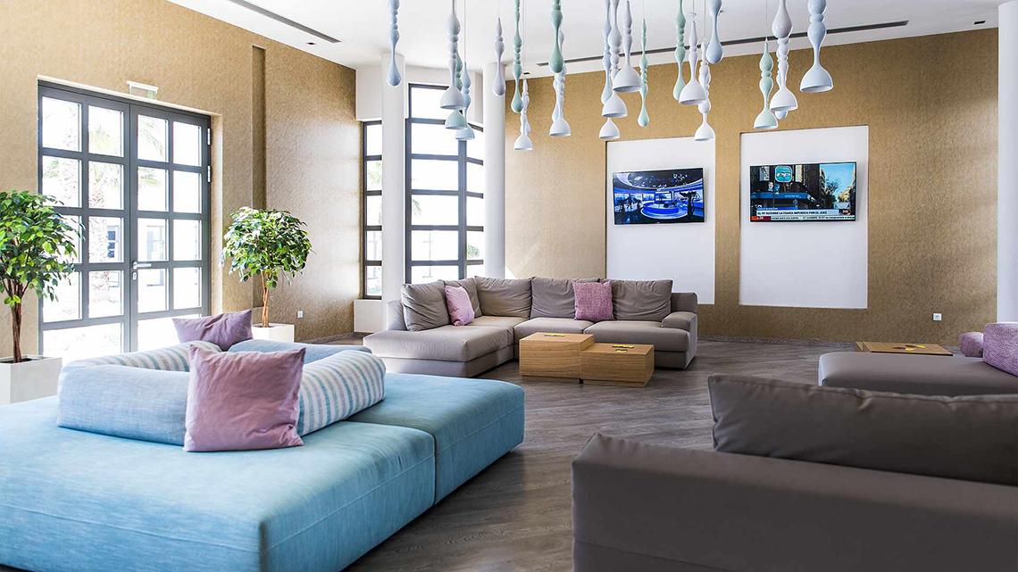 Lobby-Lounge des Club Plimmiri Hotels mit Sofas, Fernsehern und Pflanzen.