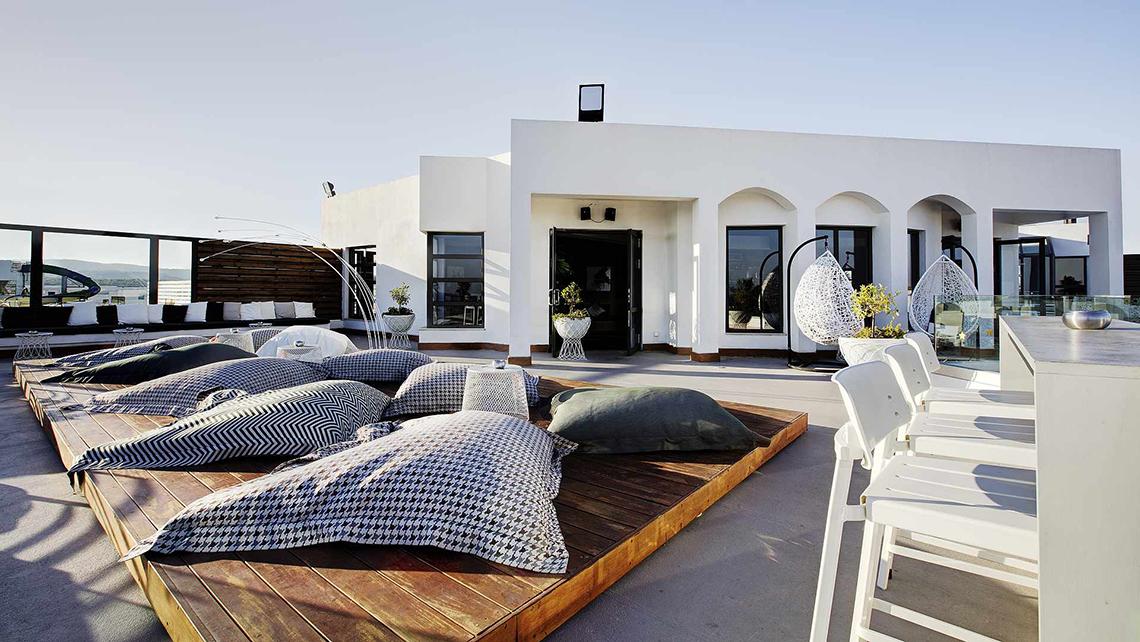 Die Dachterrasse des Club Plimmiri Hotels mit weißen Möbeln und Kissen, umgeben von Pflanzen.