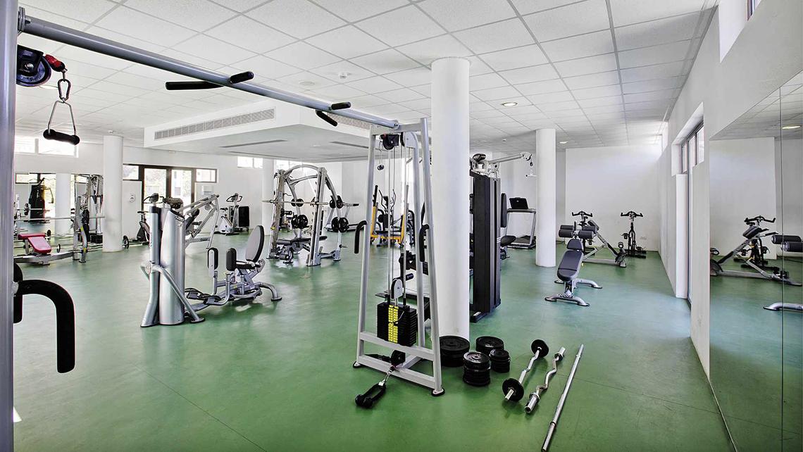 Fitnessstudio im Club Plimmiri Hotel mit verschiedenen Trainingsgeräten und grün glänzendem Boden.