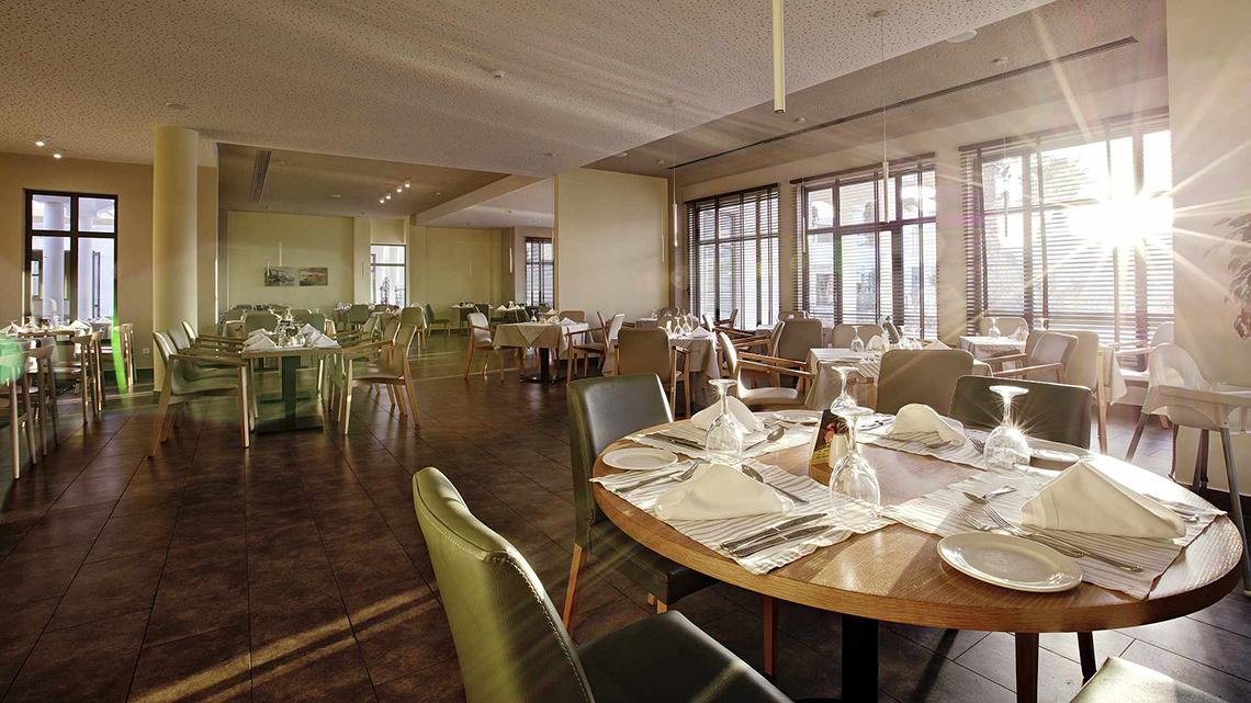 Innenansicht des Restaurants im Club Plimmiri Hotel mit runden Tischen, Stühlen und Sonnenlicht.