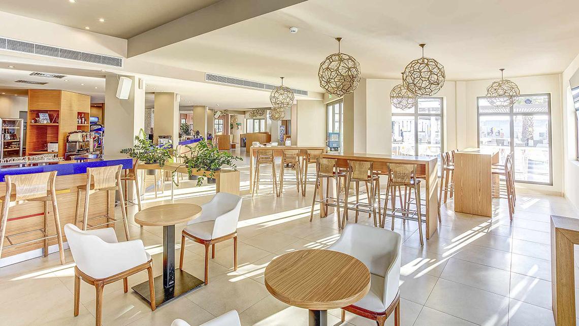 Innenbereich des Club Plimmiri Hotels mit Tischen, Stühlen und Pflanzen.
