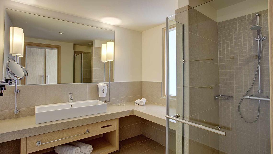 Badezimmer im Club Plimmiri Hotel mit Spiegel, Waschbecken, Dusche und Handtüchern.
