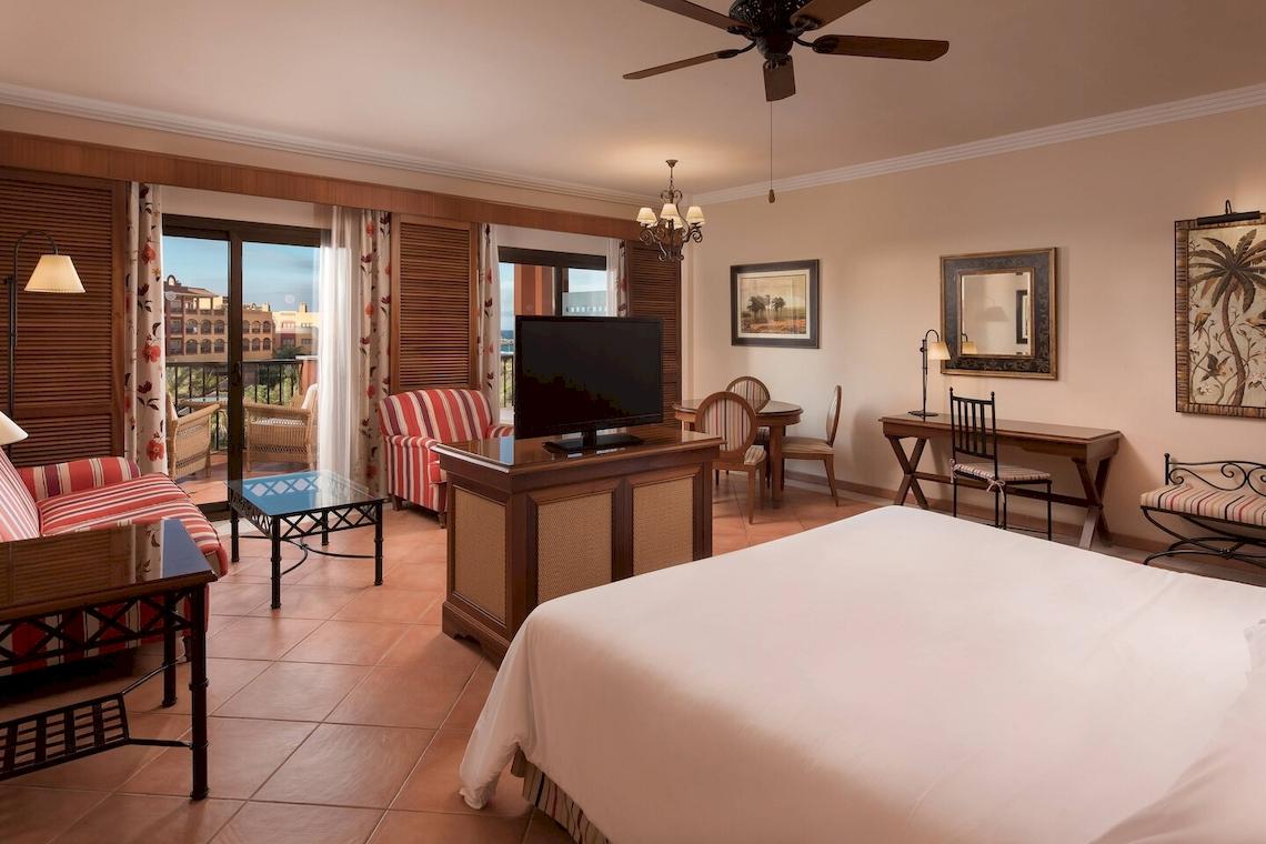 Schlafzimmer im Sheraton Fuerteventura Beach, Golf & Spa Resort mit Fernseher, Couch, Tisch und Möbeln.