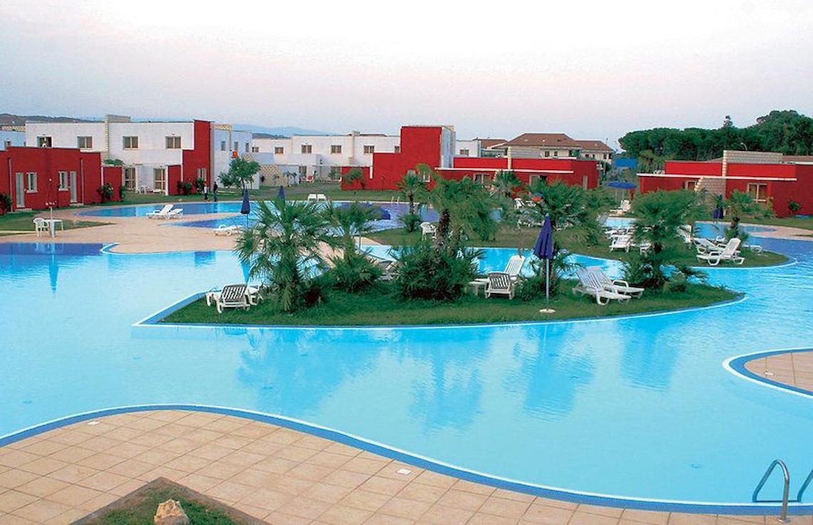 Außenpool des Club Esse Sunbeach Village Hotels mit Liegestühlen und roten Gebäuden im Hintergrund.