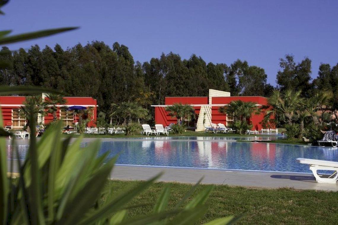 Außenbereich des Club Esse Sunbeach Village mit Pool und roten Gebäuden.
