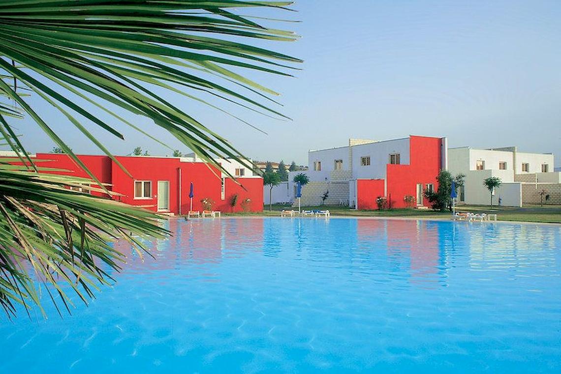 Ein großer Swimmingpool vor roten und weißen Gebäuden im Club Esse Sunbeach Village.