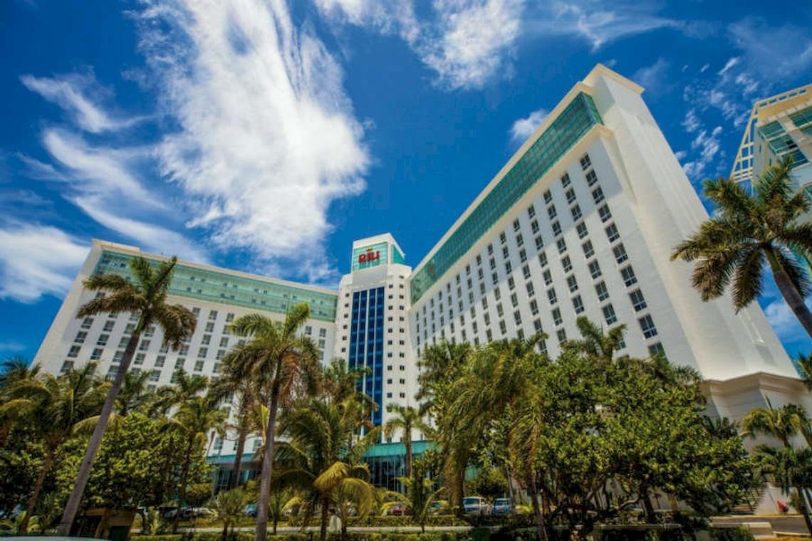 Außenansicht des Riu Cancun Hotels mit vielen Fenstern und Palmen davor.