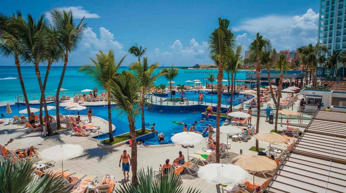 Luftaufnahme des großen Pools im Riu Cancun Hotel mit vielen Gästen und Palmen.