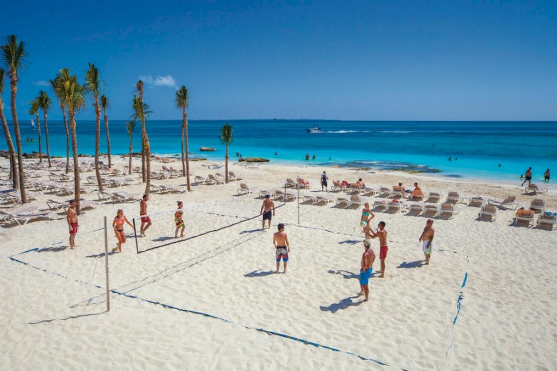 Volleyballspiel auf dem Strand des Riu Cancun Hotels mit Teilnehmern und Palmen im Hintergrund.
