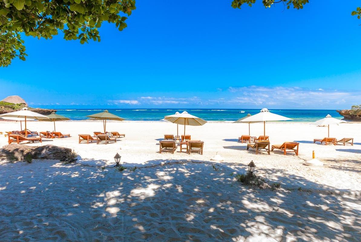 Strandszene im The Sands at Chale Island Resort mit weißen Sonnenschirmen und Holzliegen.