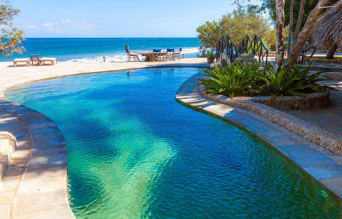 Außenpool des Sands at Chale Island Resort mit Blick auf das Meer und Liegestühlen.