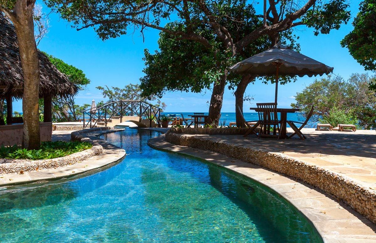 Außenpool des Sands at Chale Island Resort mit Tischen und Sonnenschirmen.