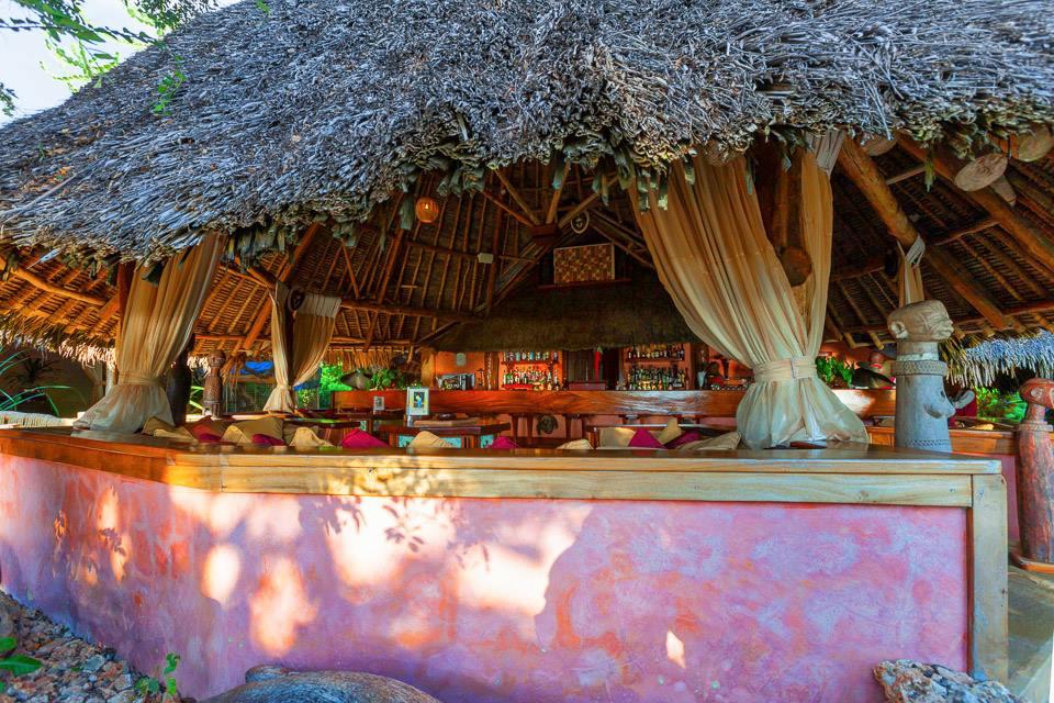 Die Bar im Sands at Chale Island Resort mit blauem Strohdach und rosa Wänden.