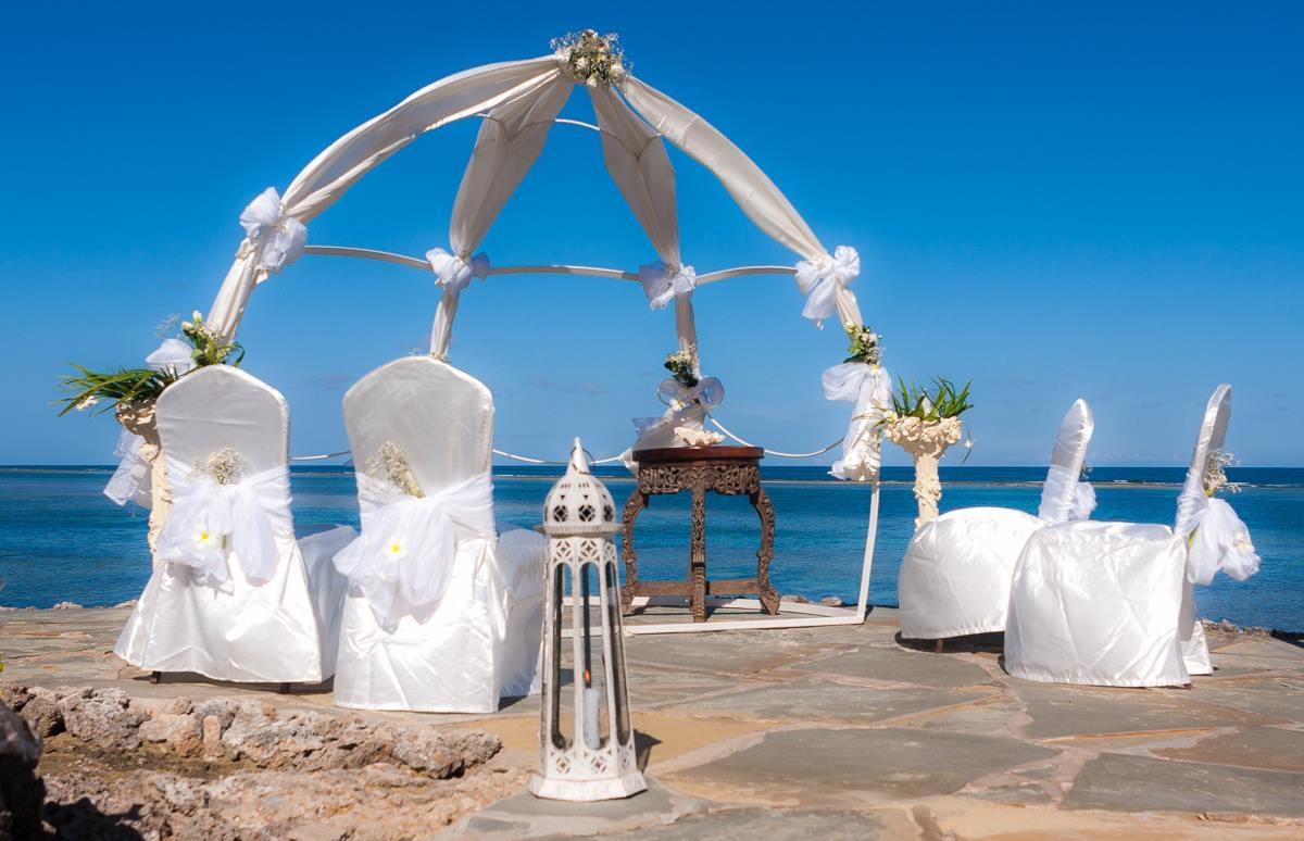 Hochzeitszeremonie am Strand vor dem Meer mit weißem Pavillon und dekorierten Stühlen.