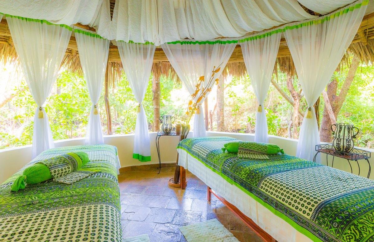 Spa-Behandlungsraum im Sands at Chale Island Resort mit zwei grünen und weißen Betten und großen Fenstern.