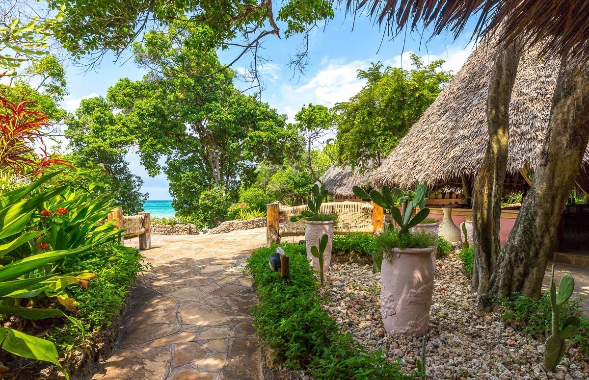 Gartenweg mit Blick auf das Meer, Hutdach und Pflanzenkübel im Sands at Chale Island Resort.
