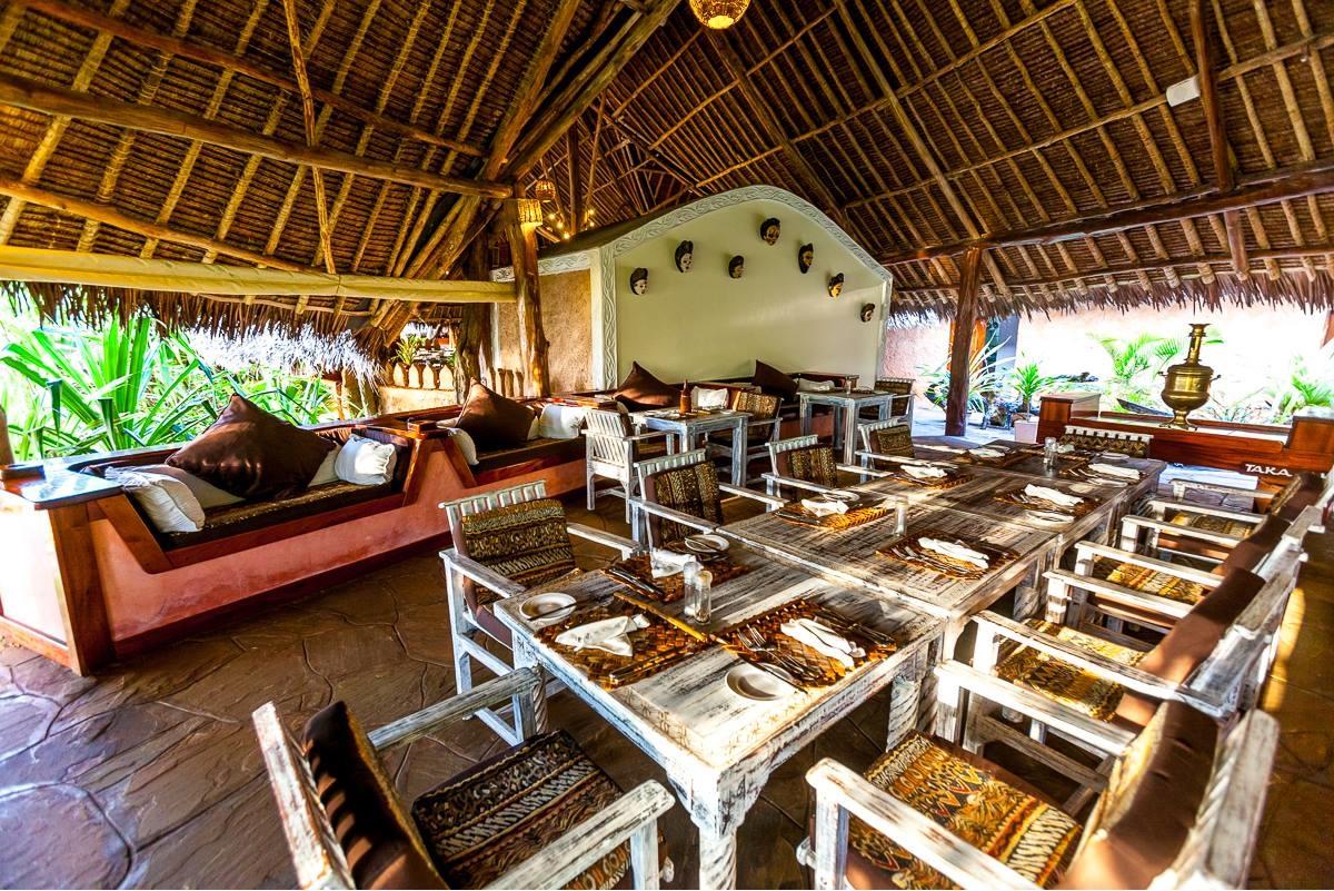 Innenbereich des Sands at Chale Island Resort mit runden Tischen, Stühlen und Kissen.
